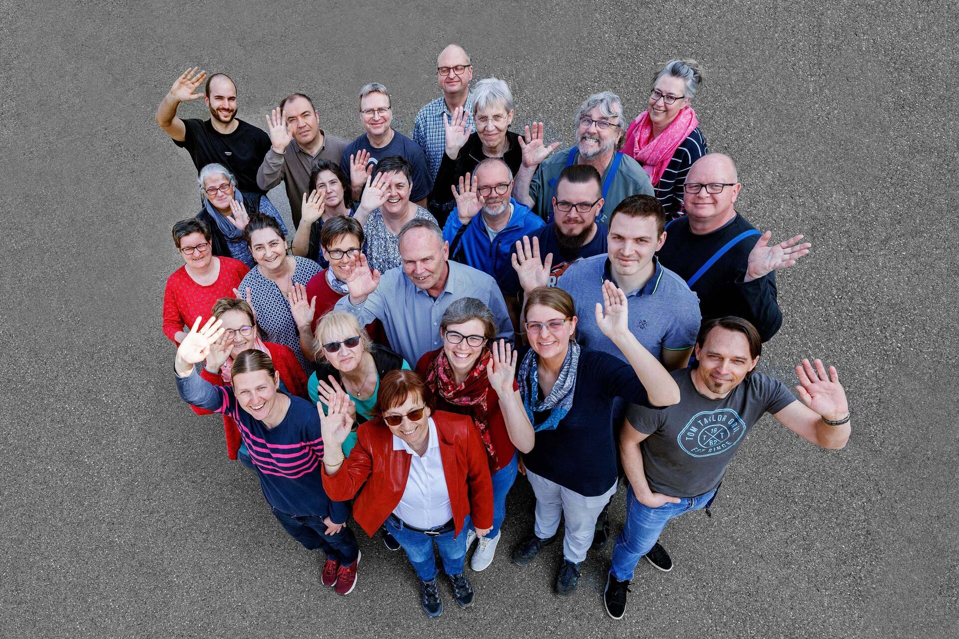 ITVP employees stand on an asphalted area and wave at the camera taking pictures from above