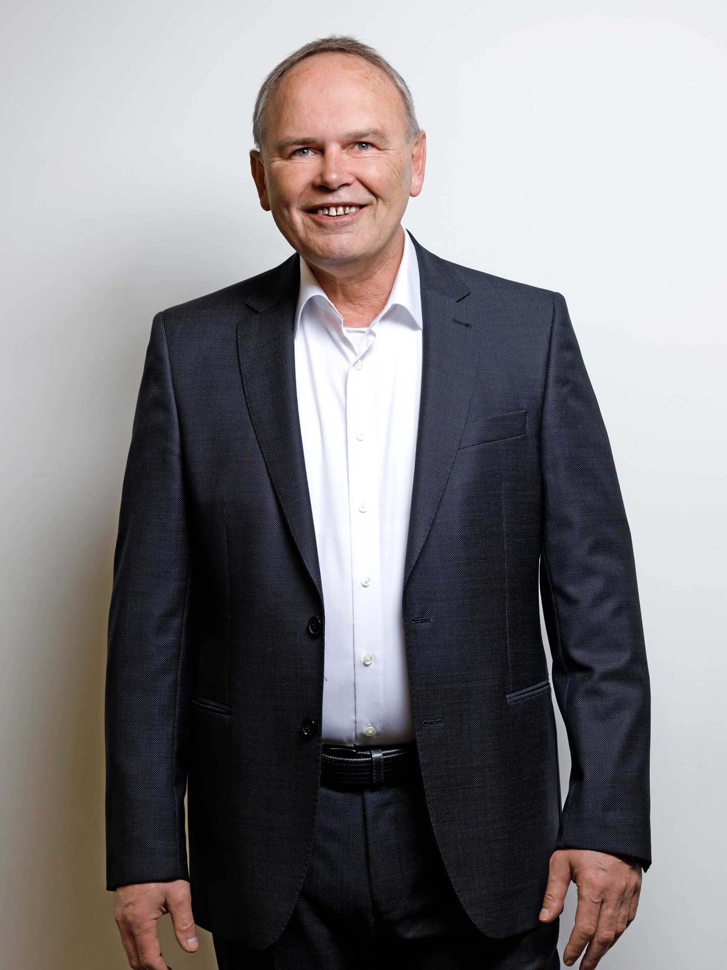 Sven trägt ein weißes Hemd und einen schwarzen Anzug. Er steht frontal zur Kamera und lächelt.