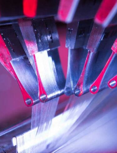 Detail of a textile machine illuminated with pink light.