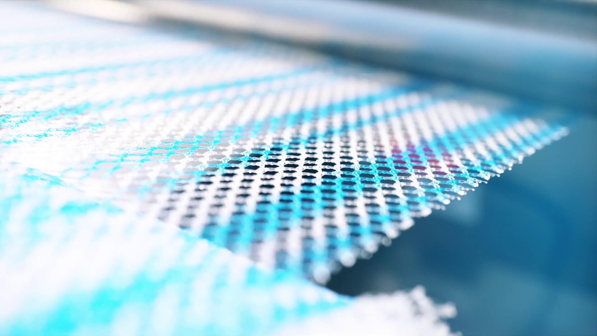 Shown is a section of mesh, with violet and white stripes, unrolled from a roll and fed into a machine.